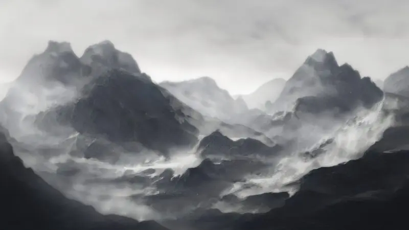 A panoramic view of a mountain range enveloped in mist and clouds, with rugged peaks and valleys partially obscured by the fog.